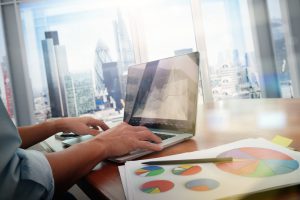 business documents on office table with smart phone and laptop computer and graph business with social network diagram and man working in the background