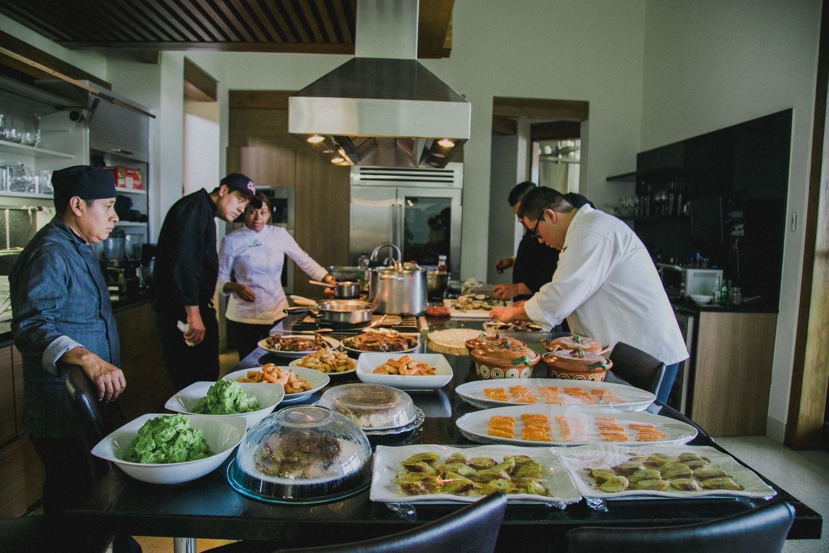 Chefs prepare multiple dishes around a fully stocked commercial kitchen island