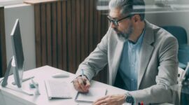 Business executive writing notes beside a desktop computer